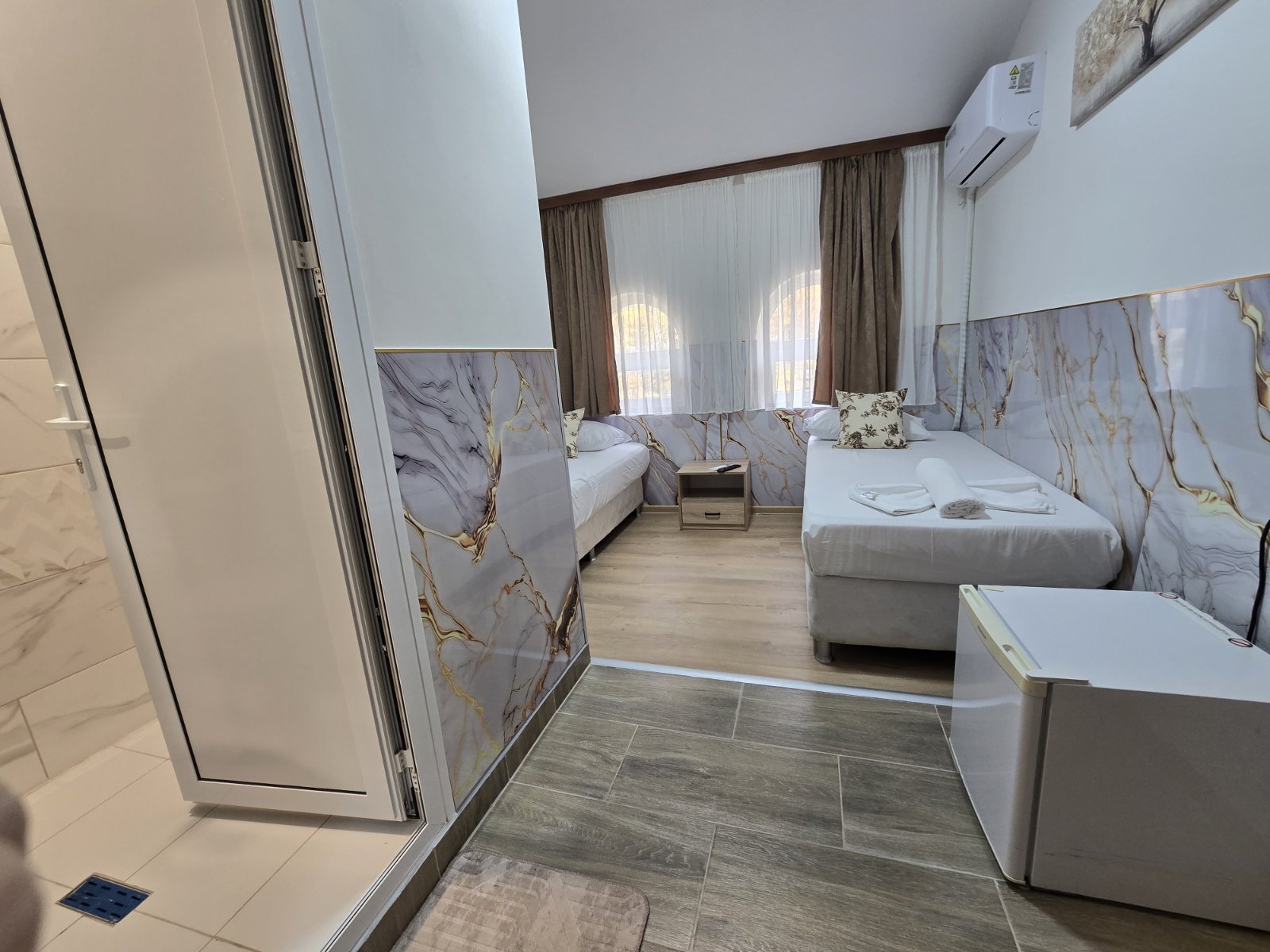 Twin hotel room with two beds, marble-patterned wall panels, and a small bedside table between them.