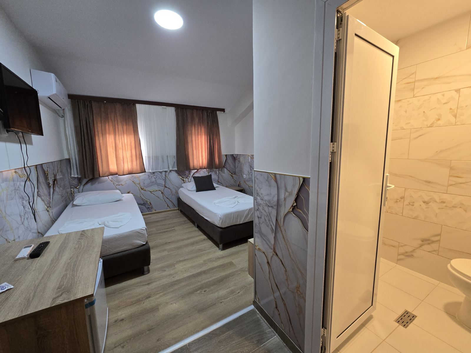 Hotel room with two single beds, white linens, and marble-patterned wall panels beneath brown curtains.